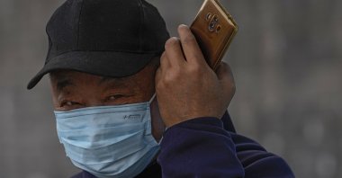 A man wearing a face mask to help curb the spread of the coronavirus listens to his smartphone on a street in Beijing, China, Oct. 28, 2021. (AP Photo)