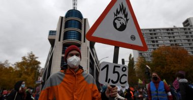 An activist holds up a placard showing a burning planet Earth and making reference to the 2015 Paris Agreement to limit global warming to 1.5 degrees Celsius (2.8 degrees Fahrenheit), in Berlin, Germany, Oct. 22, 2021. (AFP Photo)