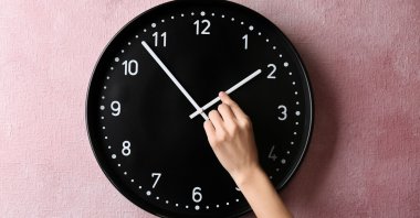 A photo showing a person changing the time on a wall clock. (Shutterstock Photo)