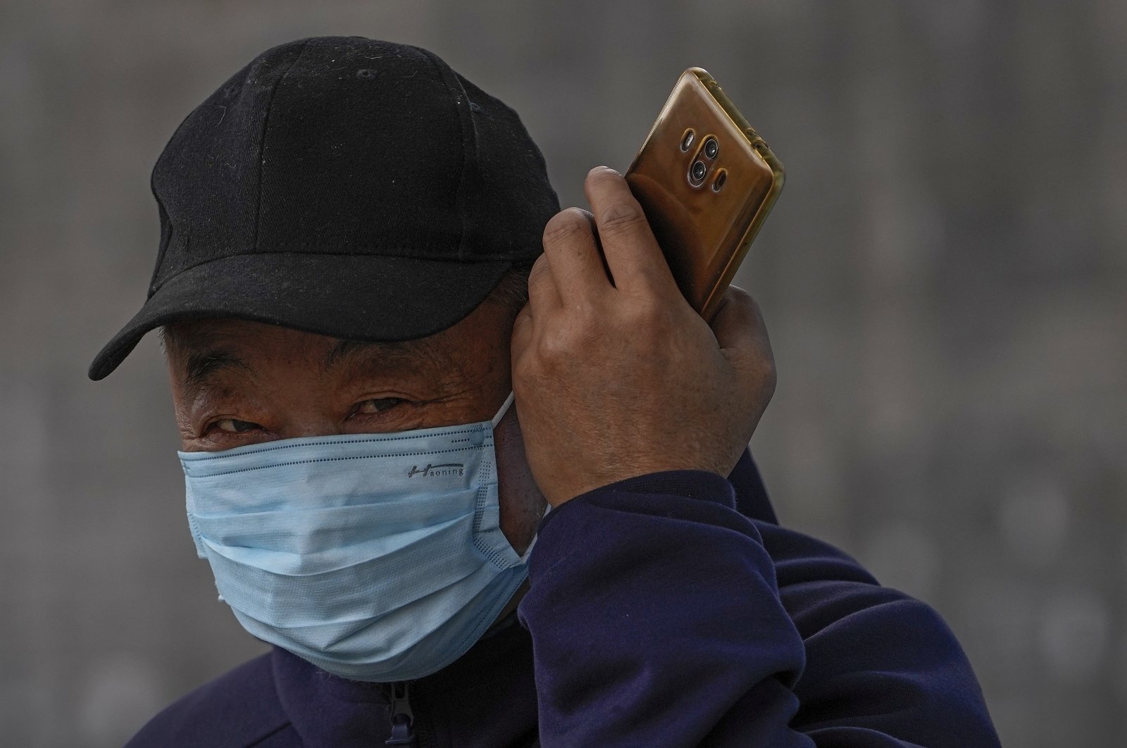 A man wearing a face mask to help curb the spread of the coronavirus listens to his smartphone on a street in Beijing, China, Oct. 28, 2021. (AP Photo)