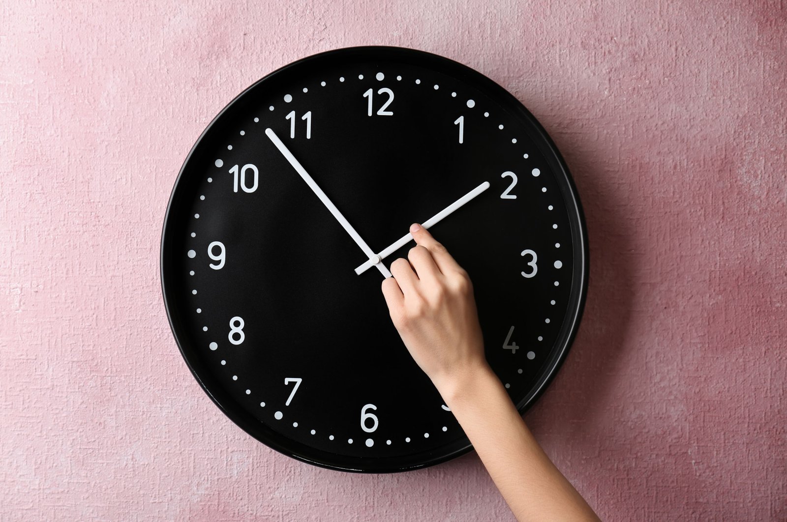 A photo showing a person changing the time on a wall clock. (Shutterstock Photo)