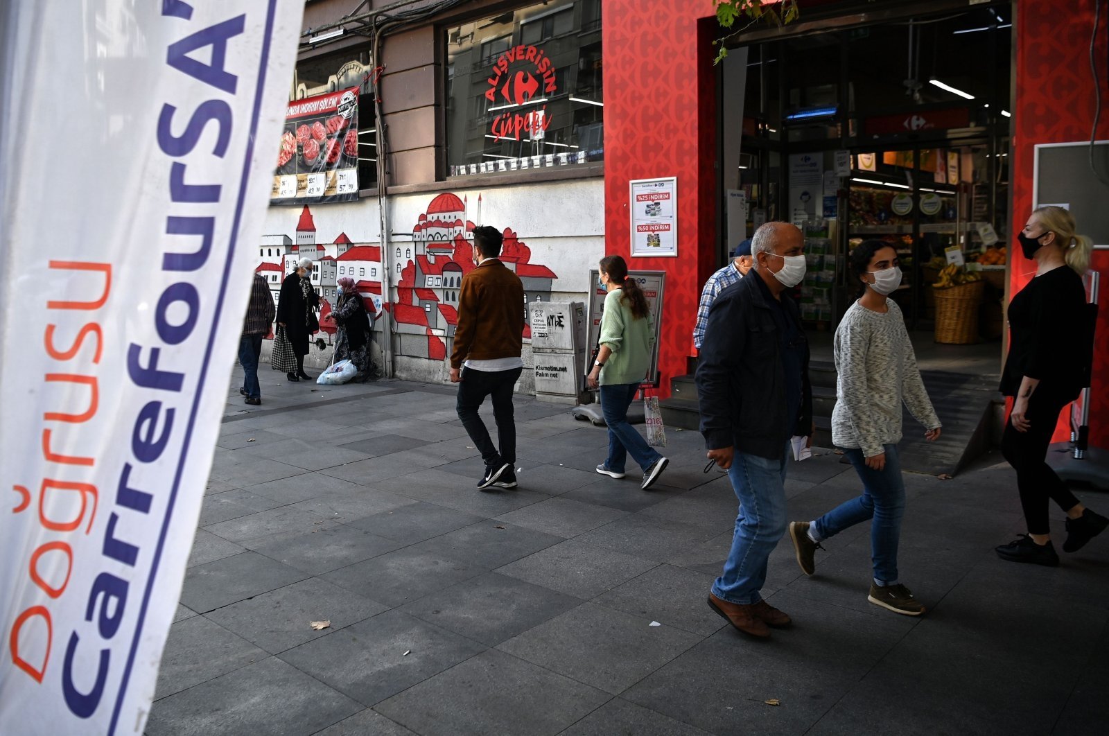 People wearing face masks walk in front of a French brand supermarket "Carrefour" at Nişantaşı district in Istanbul, Turkey, Oct. 26, 2020. (AFP Photo)