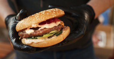 A photo showing a person wearing plastic gloves and holding a burger in hand. (Photo by Shutterstock)
