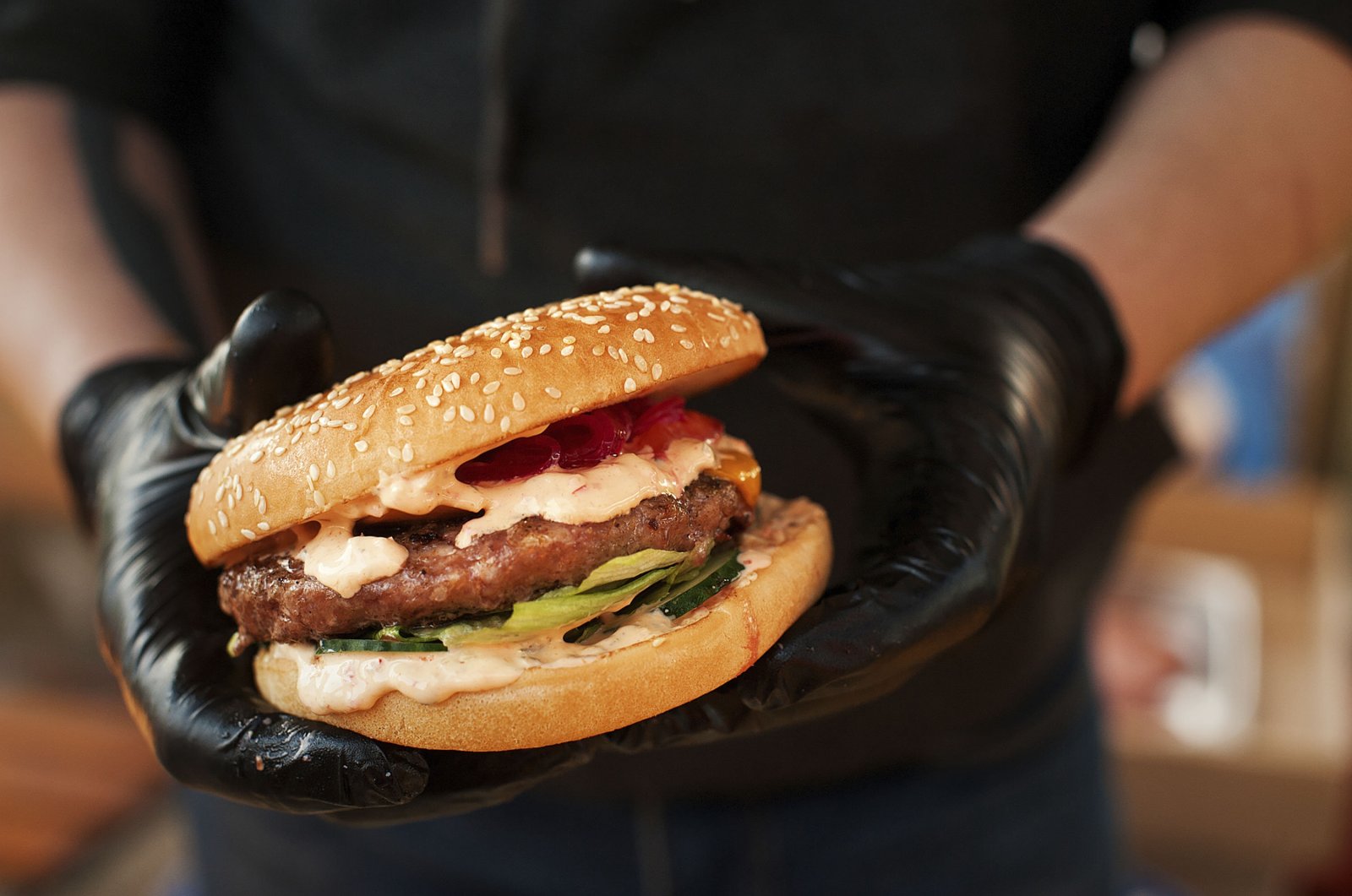 A photo showing a person wearing plastic gloves and holding a burger in hand. (Photo by Shutterstock)