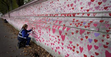Volunteer Amanda Herring who lost her brother Mark to COVID-19, writes inscriptions on the COVID-19 memorial wall in Westminster in London, U.K., Oct. 15, 2021. (AP Photo)