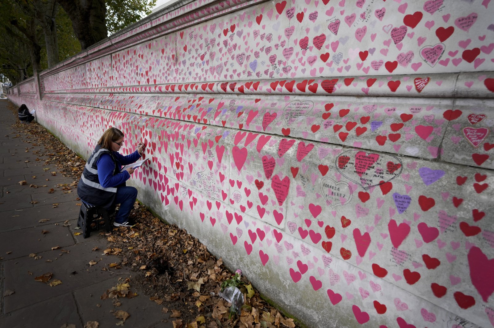 Volunteer Amanda Herring who lost her brother Mark to COVID-19, writes inscriptions on the COVID-19 memorial wall in Westminster in London, U.K., Oct. 15, 2021. (AP Photo)