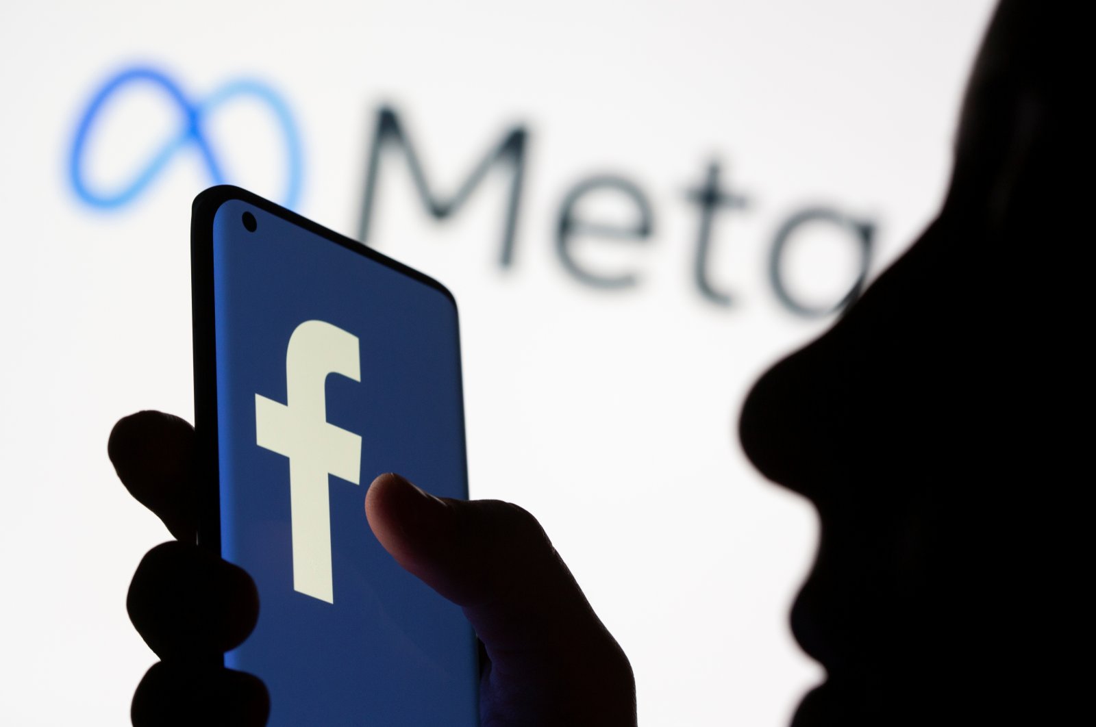 Woman holds smartphone with Facebook logo in front of Facebook's new rebrand logo Meta in this illustration picture taken Oct. 28, 2021. (REUTERS)