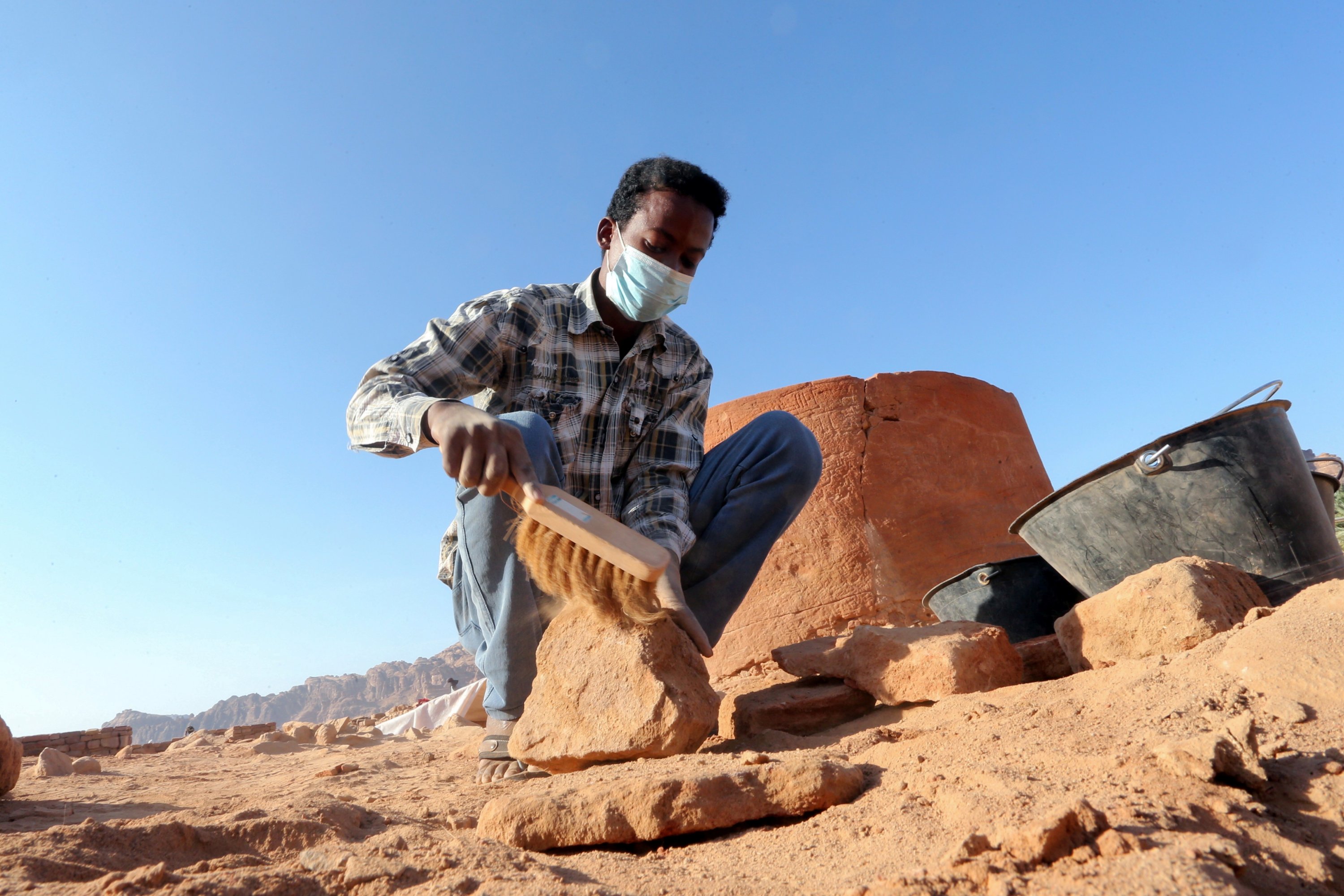 Seorang arkeolog dengan hati-hati membersihkan tembikar untuk memeriksa temuan yang diketahui berasal dari peradaban Dadan dan Lihyan tertanggal 1.000 SM, Al-Ula, Arab Saudi, 30 Oktober 2021. (Foto Reuters)