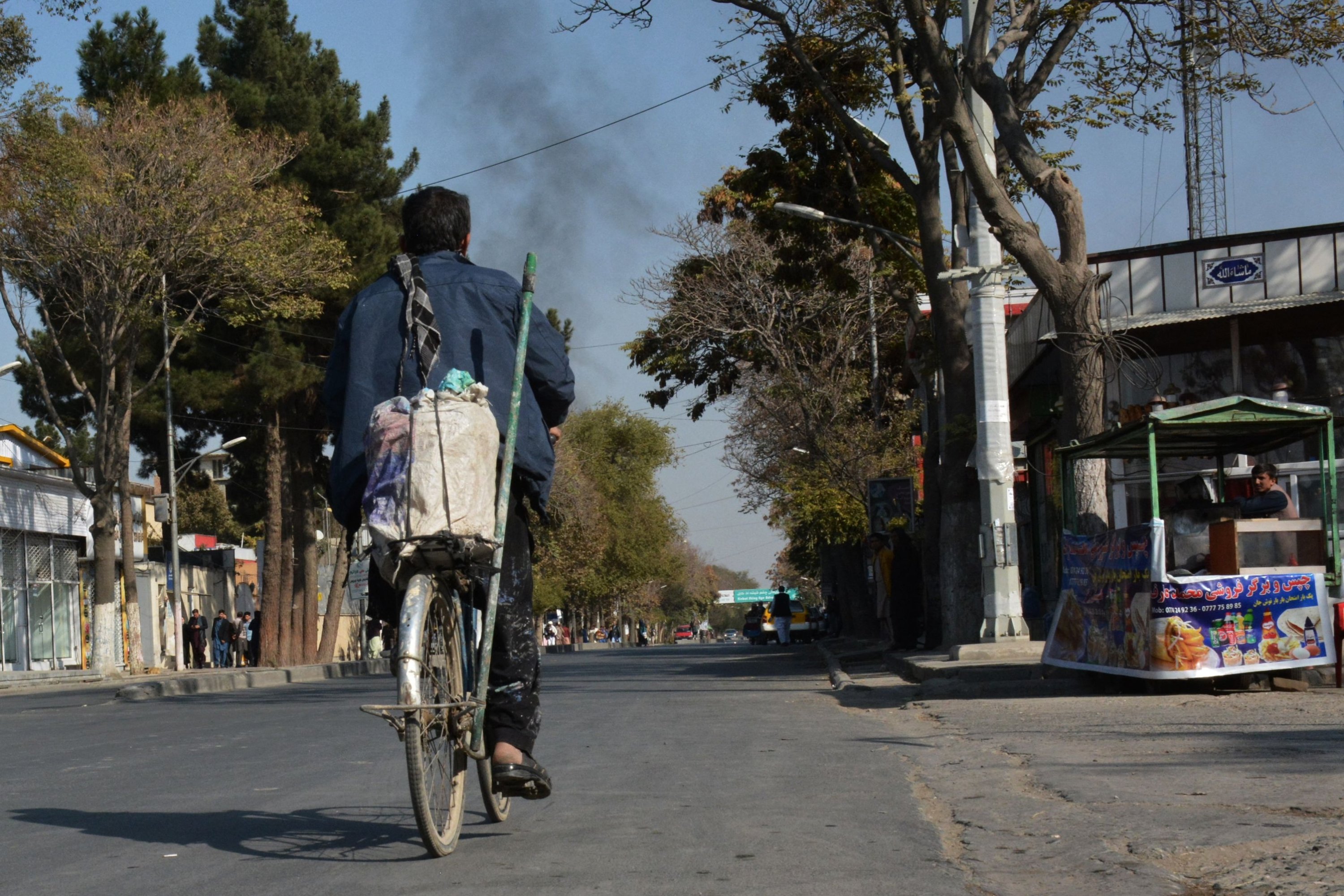 An Afghan man rides a bicycle along a road against the backdrop of smoke rising from the site of blasts in Kabul, Afghanistan, Nov. 2, 2021. (AFP Photo)