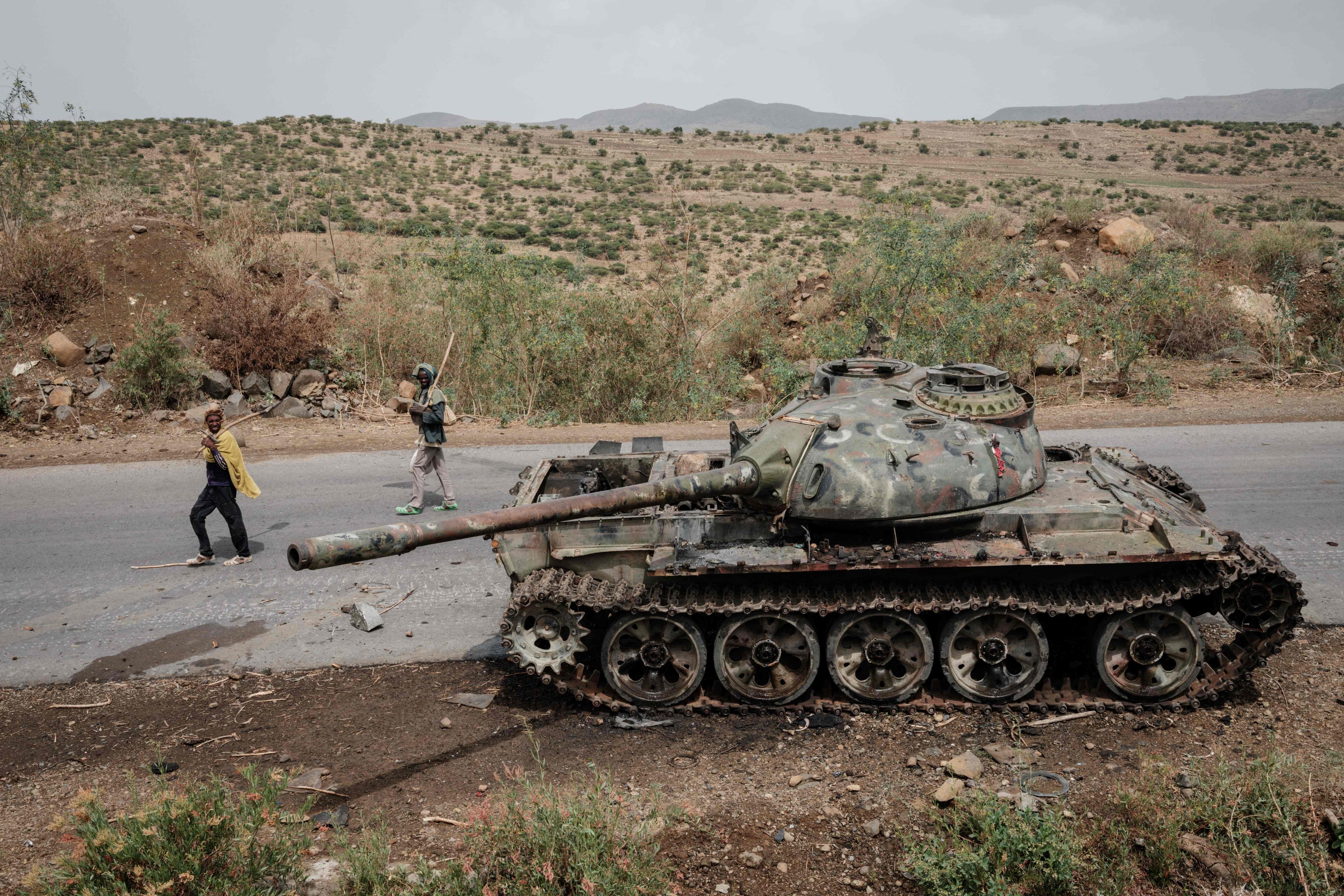 Local farmers walk next to a damaged tank that is abandoned along the road in this file photo taken in Dansa, southwest of Mekele in Tigray region, Ethiopia, June 20, 2021. (Photo by Yasuyoshi CHIBA / AFP)