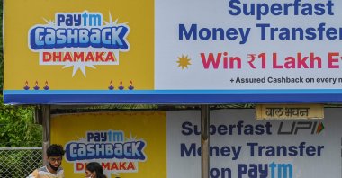 A family sits next to a billboard advertisement for Paytm, an Indian cellphone-based digital payments platform, in Mumbai, India, Nov. 7, 2021. (AFP Photo)