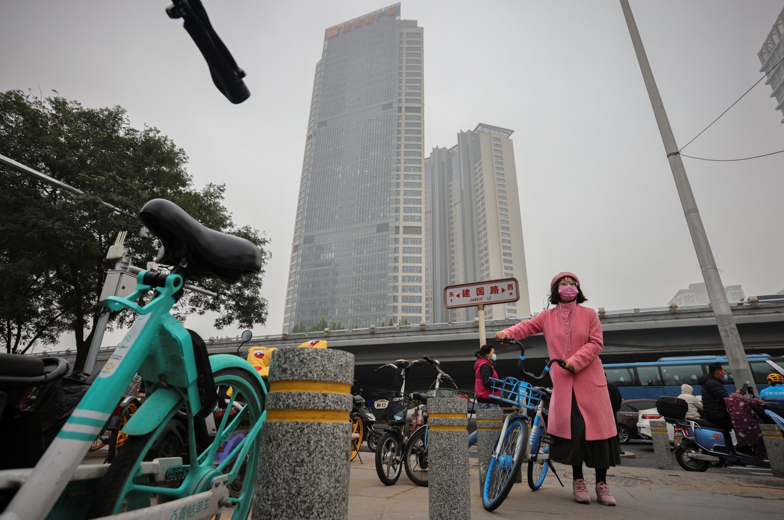A woman pushes a bike in front of the Kaisa Plaza developed by Kaisa Group Holdings Ltd on a hazy day in Beijing, China, Nov. 5, 2021. (Reuters Photo)