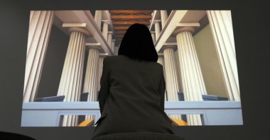 Museum supervisor Xenia Vlahou watches a video projection of the Ancient Olympia temple at the Olympic Museum in Athens, Greece, Nov. 9, 2021. (AP Photo)