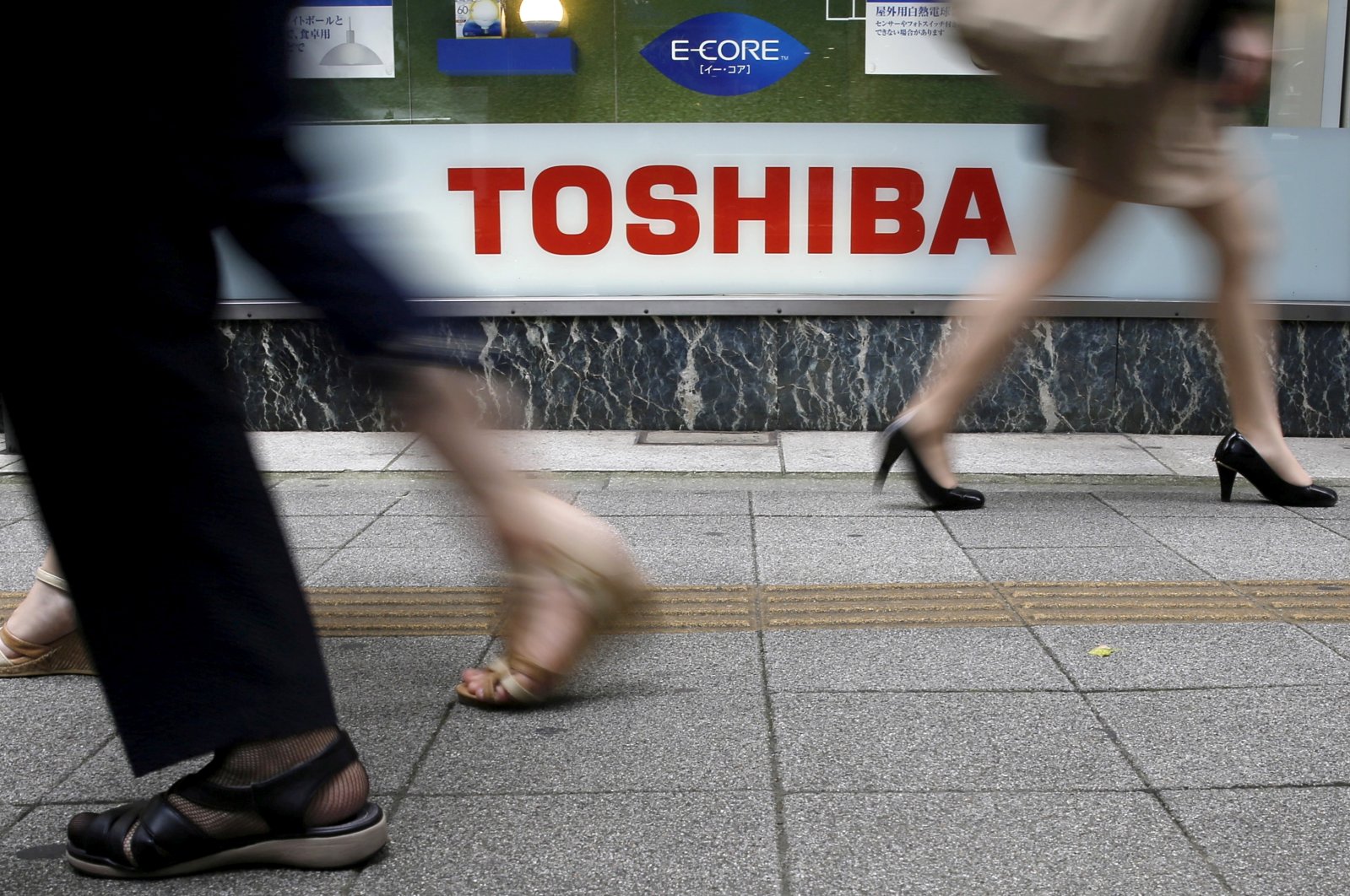 Pedestrians walk past a logo of Toshiba Corp outside an electronics retailer in Tokyo, Japan, Sept. 14, 2015. (Reuters Photo)