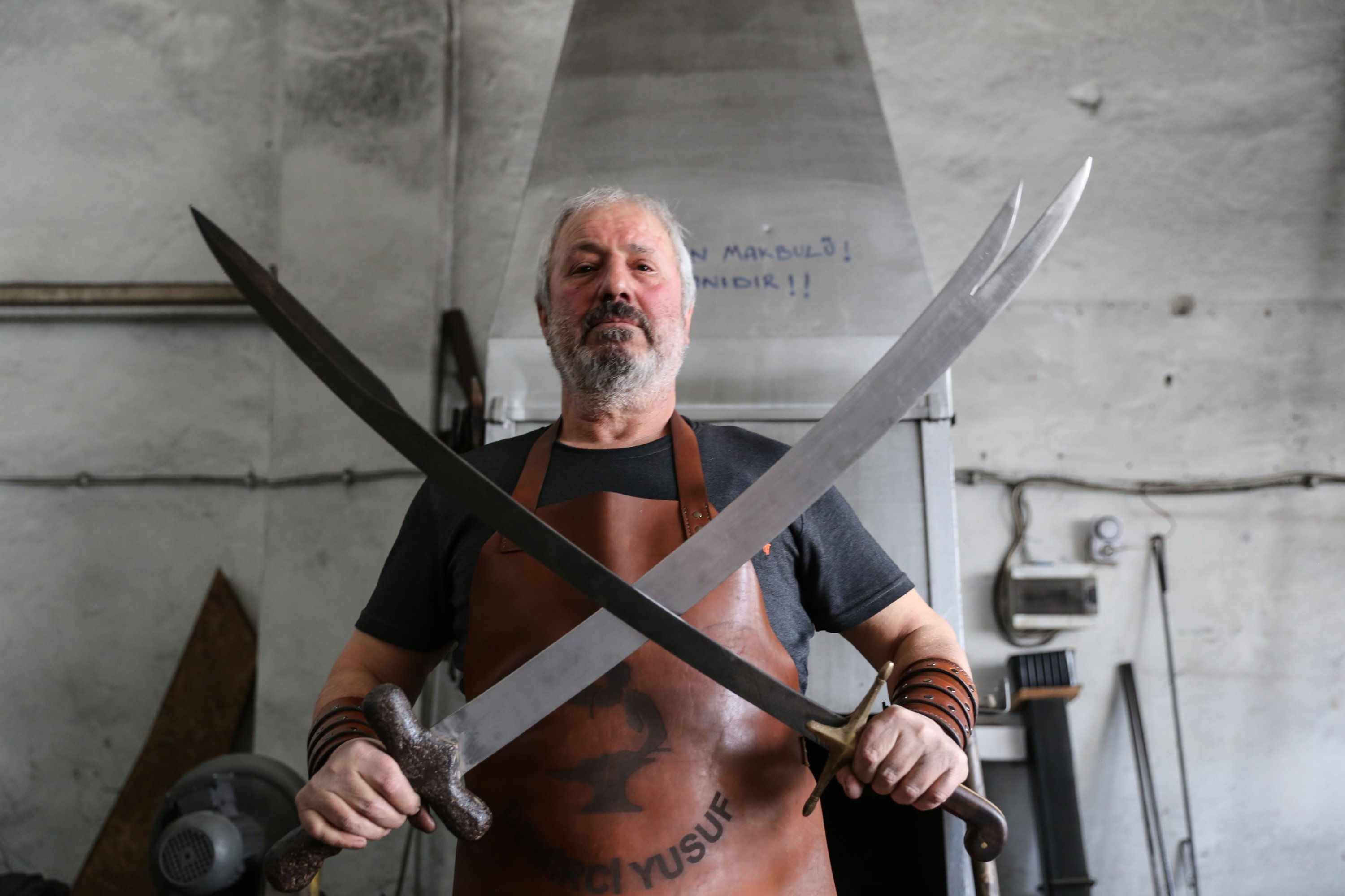 Yusuf Bayyiğit in his workshop holding two Damascus steel swords he handmade in Malatya, Turkey, Nov. 9, 2021. (AA Photo)