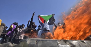 A man holds a Sudanese national flag before flames at a barricade as people protest against the military coup, east of the capital Khartoum, Sudan, Nov. 13, 2021. (AFP Photo)
