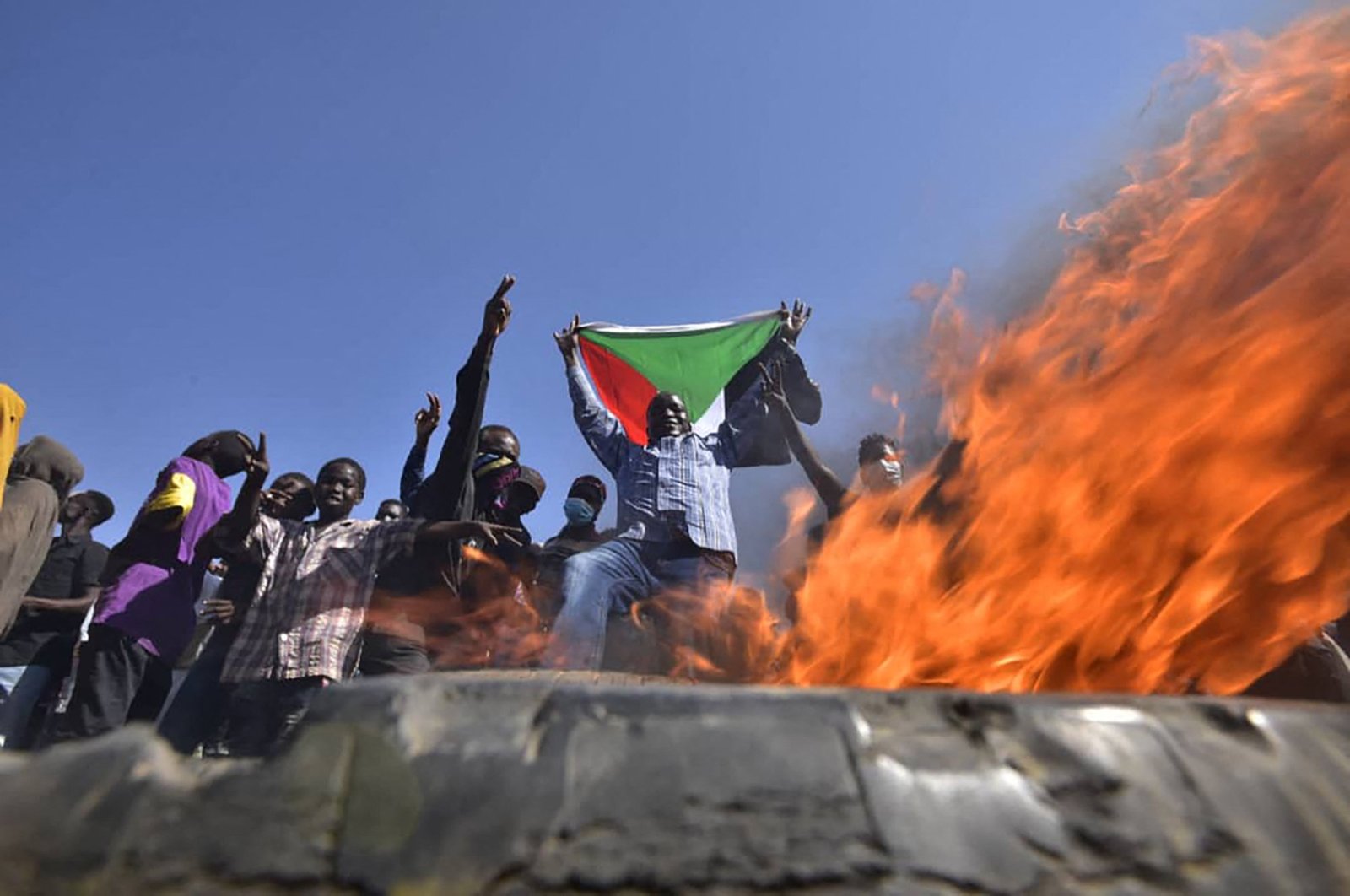 A man holds a Sudanese national flag before flames at a barricade as people protest against the military coup, east of the capital Khartoum, Sudan, Nov. 13, 2021. (AFP Photo)