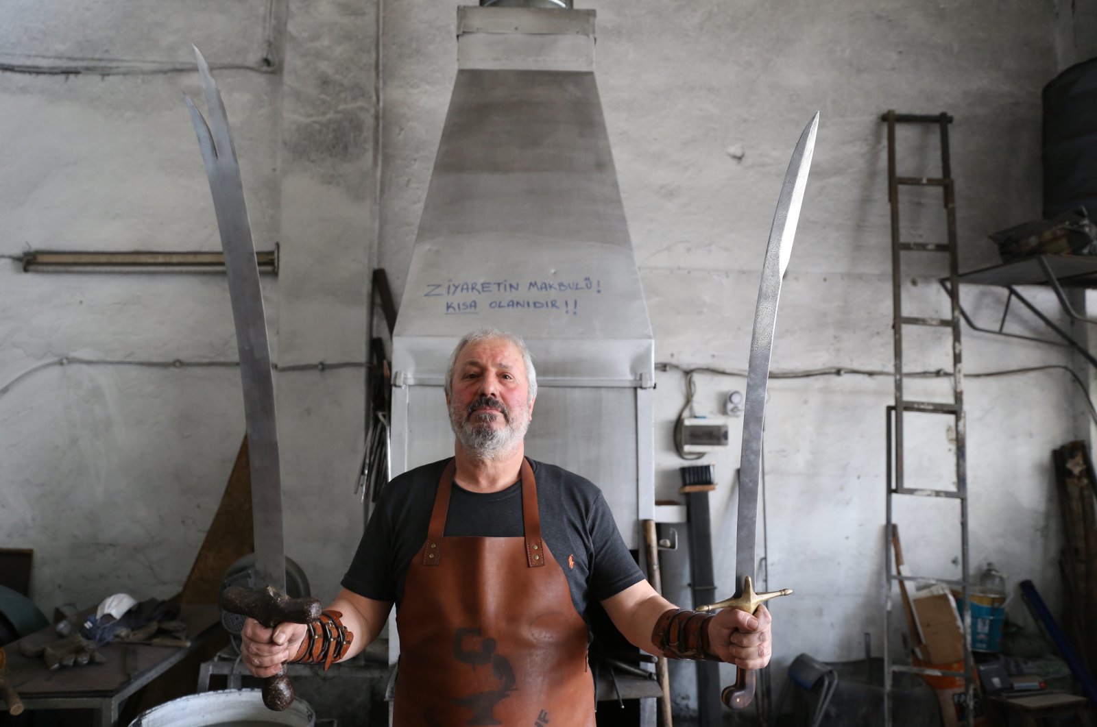 Yusuf Bayyiğit in his workshop holding two Damascus steel swords he made using traditional methods in Malatya, Turkey, Nov. 9, 2021. (AA Photo)
