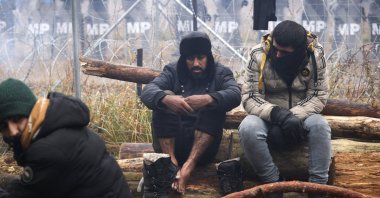 Poland's servicemen stand behind a barbed-wire fence on the Belarusian-Polish border as migrants warm at the fire, on the Belarusian side in the Grodno region on Nov. 14, 2021. (AFP Photo)
