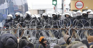 Migrants gather in front of a barbed wire fence and Polish servicemen at the checkpoint &quot;Kuznitsa&quot; at the Belarus-Poland border near Grodno, Belarus, Nov. 15, 2021. (AP Photo)