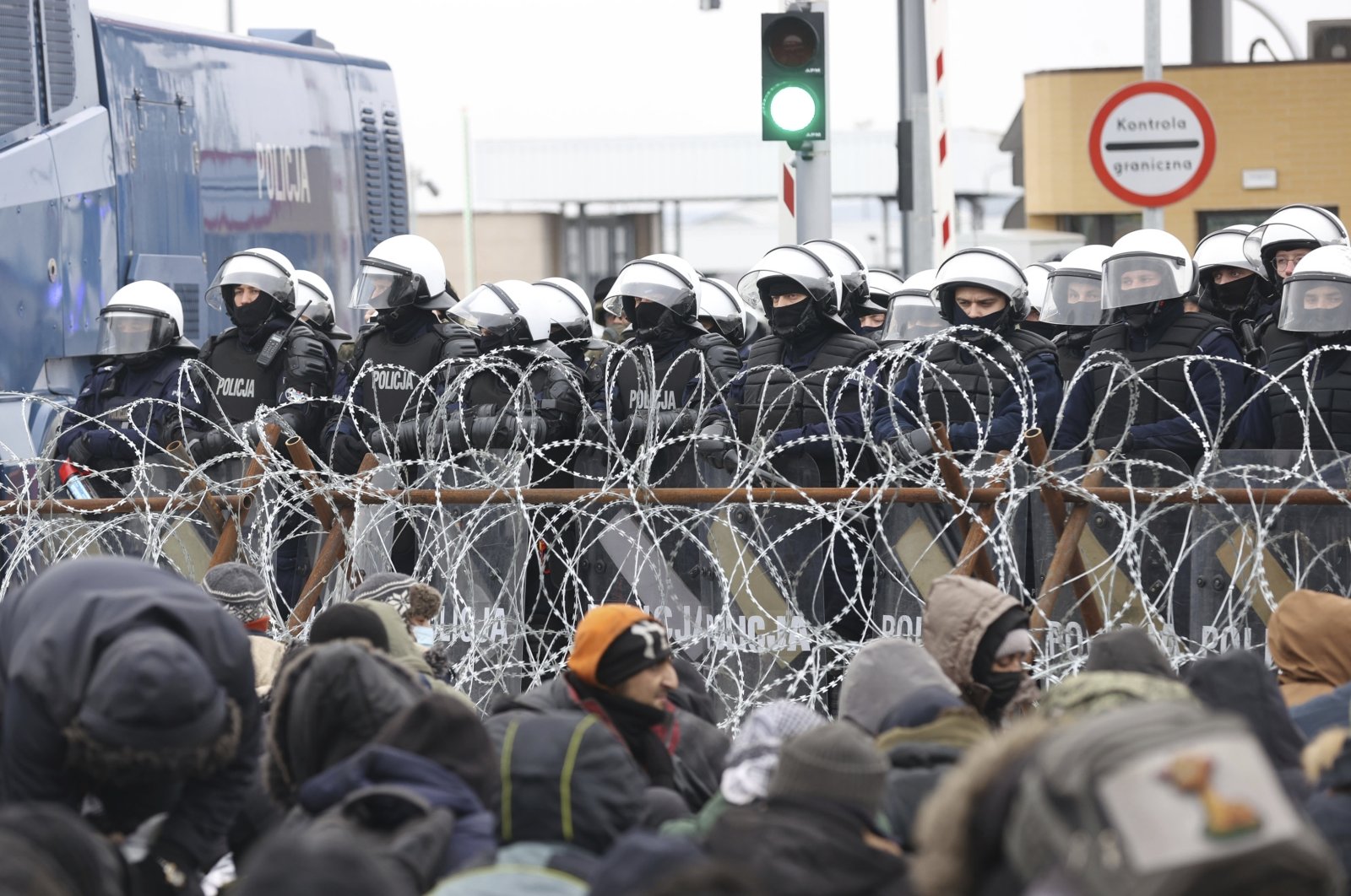 Migrants gather in front of a barbed wire fence and Polish servicemen at the checkpoint &quot;Kuznitsa&quot; at the Belarus-Poland border near Grodno, Belarus, Nov. 15, 2021. (AP Photo)