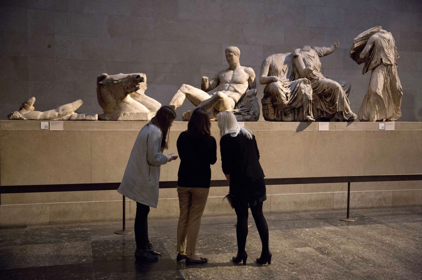 Women stand by a marble statue of a naked youth thought to represent Greek god Dionysos (C) from the east pediment of the Parthenon at the British Museum in London, Jan. 8, 2015. (AP Photo)