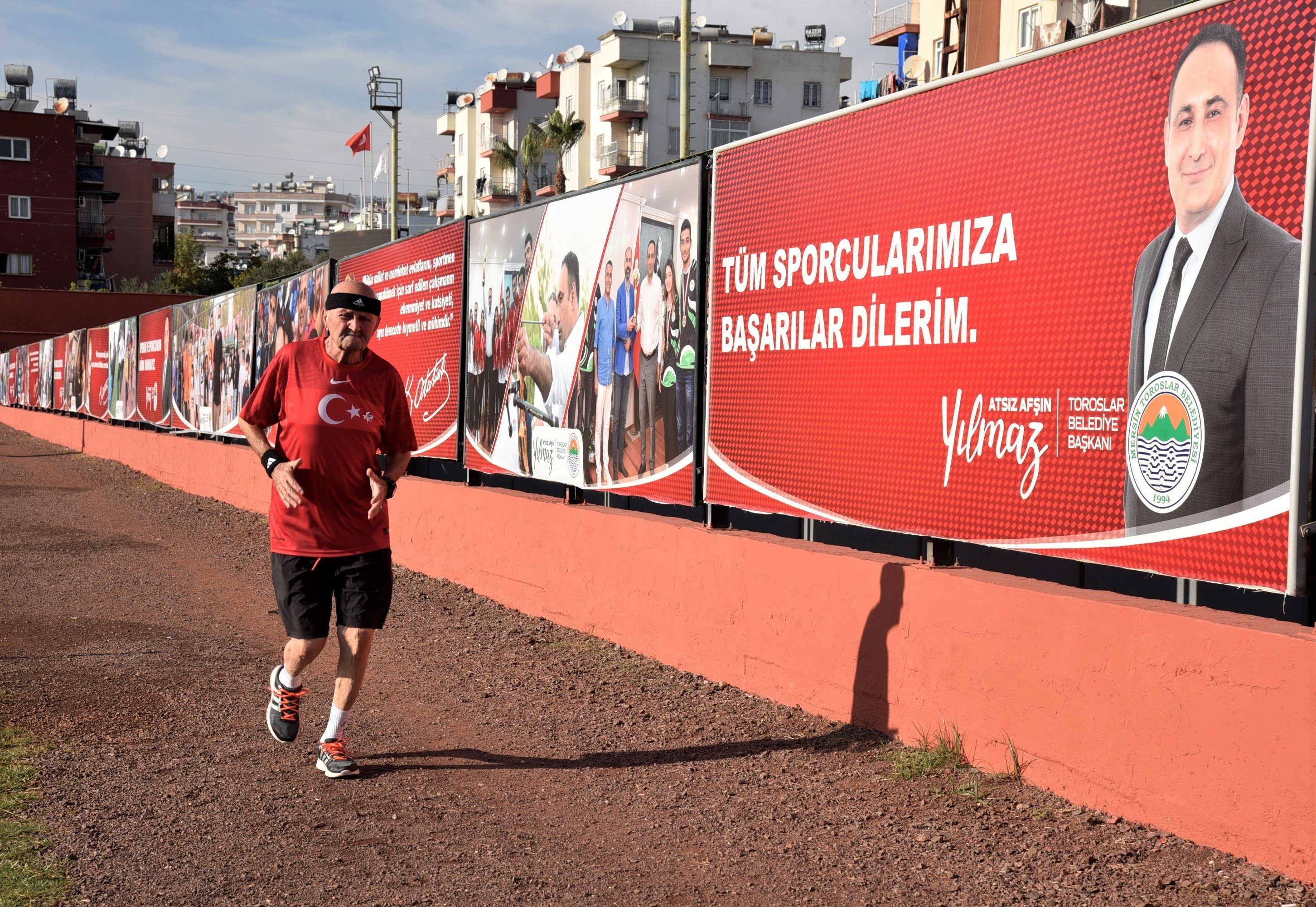 Pelari maraton Turki Ahmet Kahveci, 74, terlihat berlatih di depan poster Walikota Toroslar Atsız Afşın Yılmaz di tenggara provinsi Mersin, Turki, 10 November.  16, 2021. (Foto IHA)