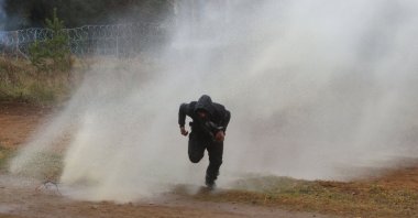 A man runs away from a water cannon used by Polish law enforcement officers against migrants attempting to break into Poland at the Bruzgi-Kuznica border crossing on the Belarusian-Polish border, Nov. 16, 2021. (AFP Photo)