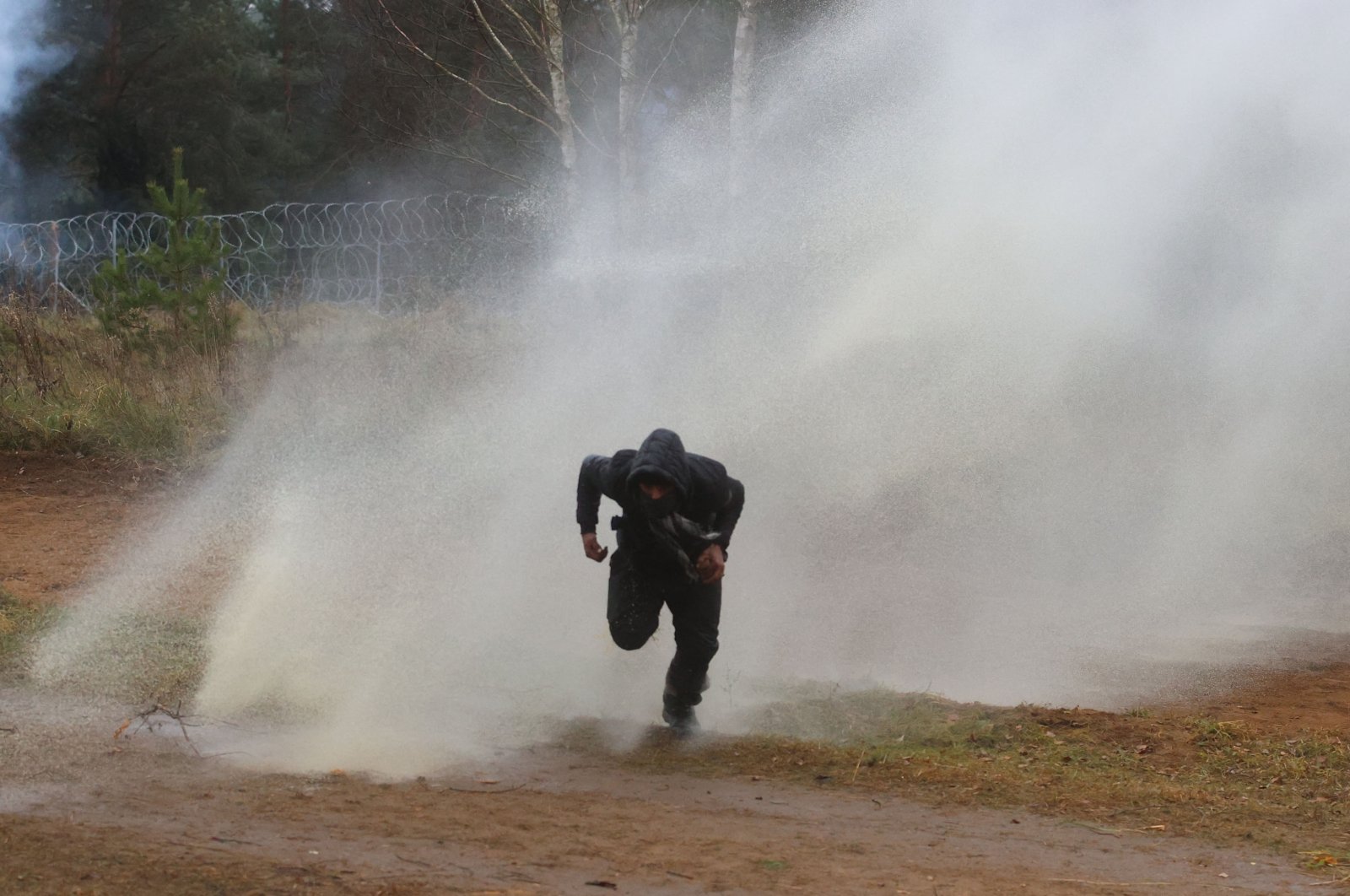 A man runs away from a water cannon used by Polish law enforcement officers against migrants attempting to break into Poland at the Bruzgi-Kuznica border crossing on the Belarusian-Polish border, Nov. 16, 2021. (AFP Photo)