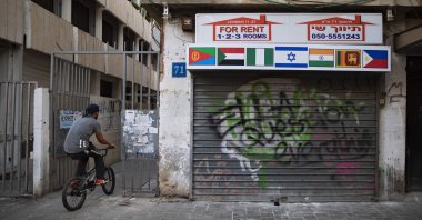 An African migrant rides his bicycle next to a closed real-estate office with the flags of Israel, Sudan and other African countries, in Tel Aviv, Israel, Oct. 23, 2020. (AP Photo)