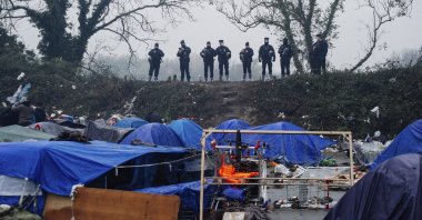 Police forces watch a makeshift migrant camp in Grande-Synthe, Northern France, Nov. 16, 2021. (AP File Photo)