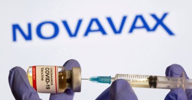 A woman holds a small bottle labeled with a "Coronavirus COVID-19 Vaccine" sticker and a medical syringe in front of displayed Novavax logo in this illustration taken, Oct. 30, 2020. (Reuters Photo)