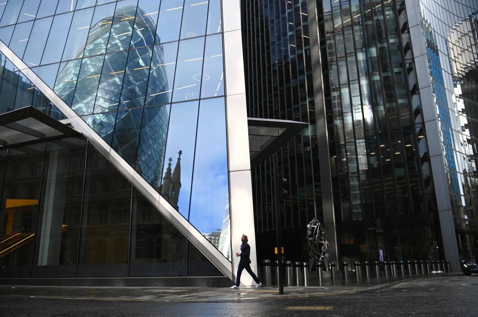 A pedestrian walks past a building with the reflection of the Gherkin in the City of London on Nov. 12, 2021. (AFP Photo)