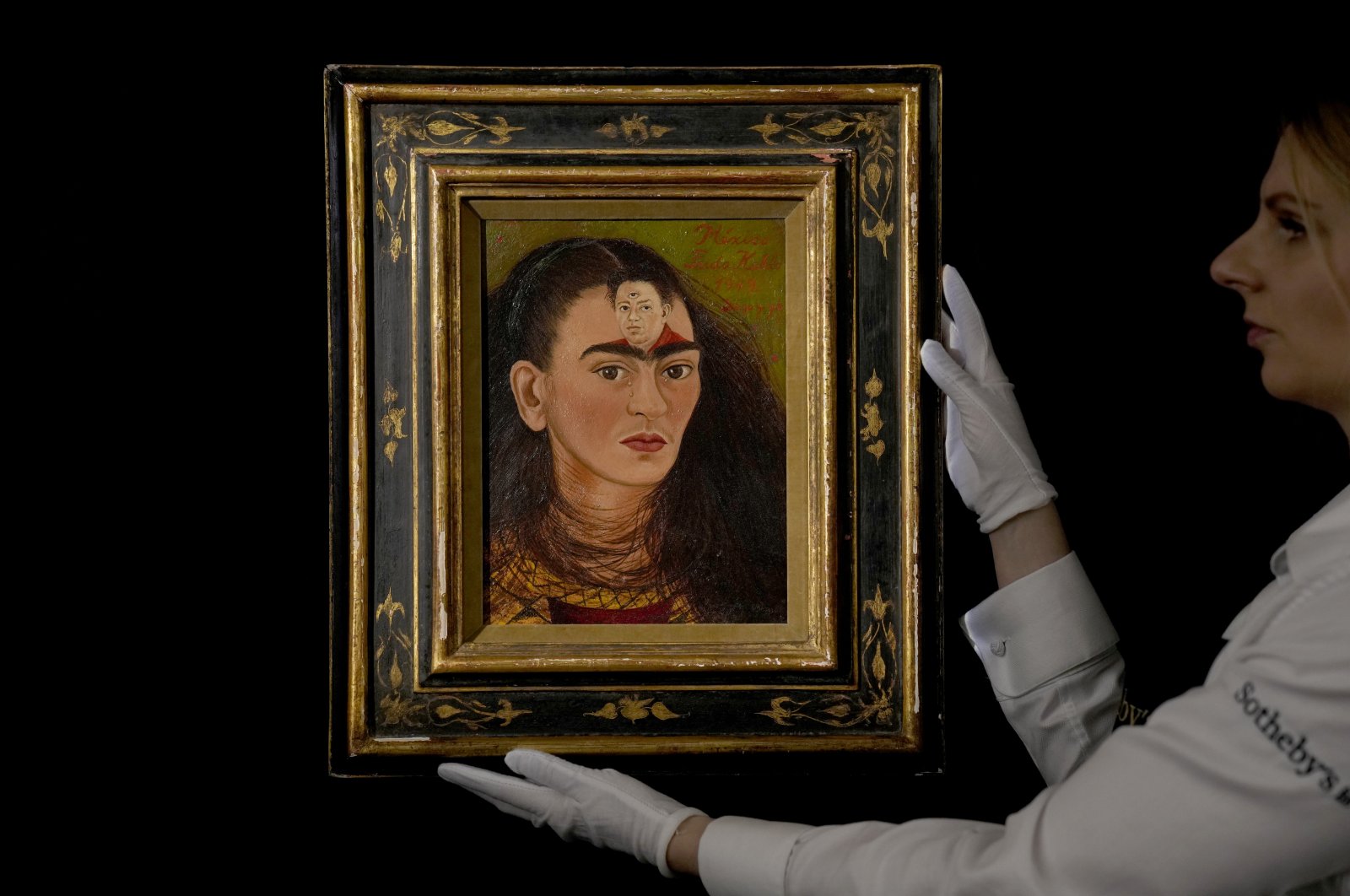 A staff member holding Frida Kahlo&#039;s 1949 self-portrait &quot;Diego y yo&quot; at Sotheby&#039;s auction house in London, U.K., Oct. 21, 2021. (AP)