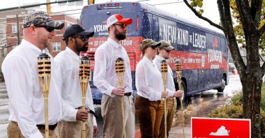A small group of demonstrators dressed as "Unite the Right" rally-goers with tiki torches stand on a sidewalk  for a campaign event in Charlottesville, Virginia, U.S., Oct. 29, 2021. (REUTERS/Jonathan Ernst)