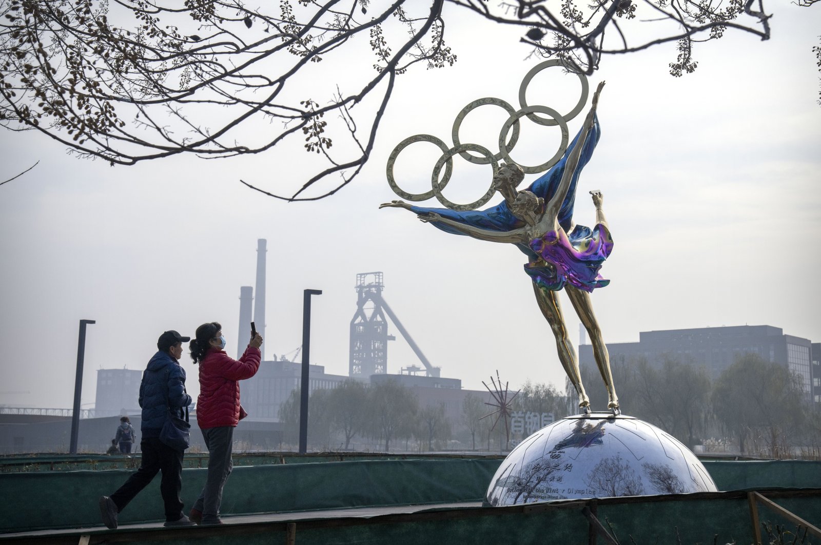 Visitors take photos of a statue of figure skaters with the Olympic rings at a park near the headquarters of the Beijing Organizing Committee for the Olympic Games (BOCOG) in Beijing, China, Nov. 18, 2021. (AP Photo)
