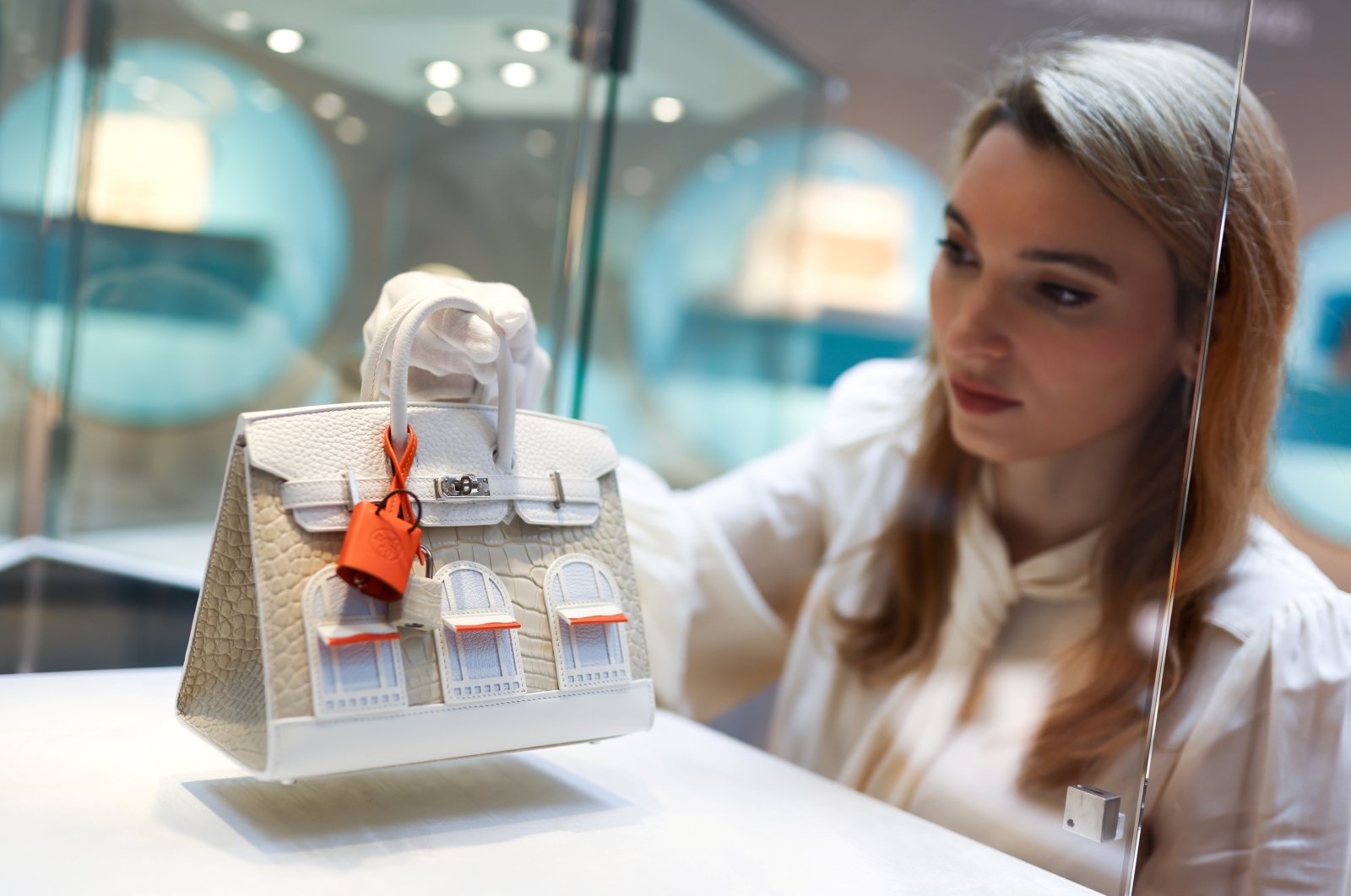 Rachel Koffsky, international senior specialist at Christie’s Handbags & Accessories, poses with a piece titled, "A rare, matte beton alligator, white togo & swift leather, orange swift leather, and bleu brume Epsom leather faubourg Sellier Birkin 20 with palladium hardware, Hermes, 2021," which is on display as part of "Handbags Online: The London Edit" at Christie&#039;s in London, Britain, Nov. 18, 2021. (REUTERS Photo)