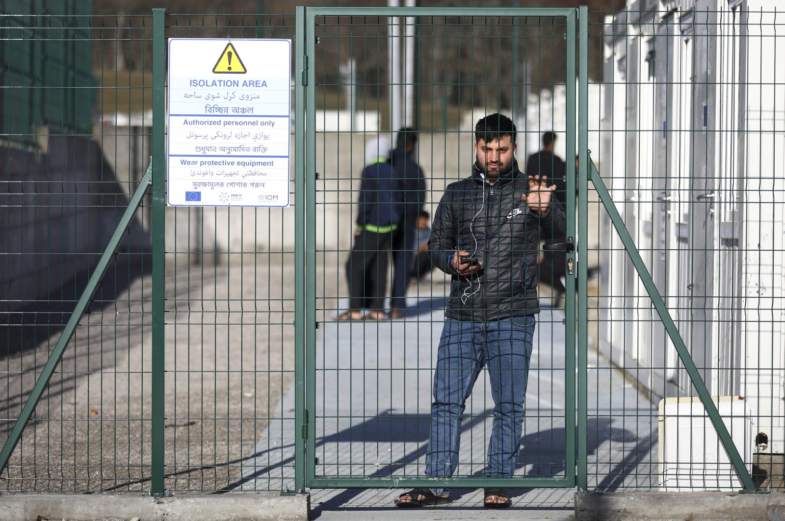 A migrant stands behind a gate at the newly built camp that was inaugurated by the European Union and International Organization for Migration officials along with Bosnian authorities near Bihac, northwestern Bosnia-Herzegovina, Nov. 19, 2021. (AP Photo)