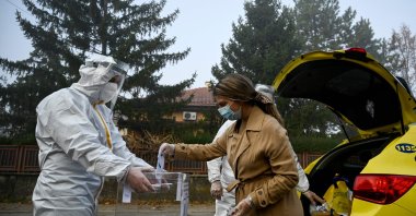 An electoral staff member of a mobile polling center, wearing Personal Protective Equipment (PPE), presents a ballot box to a woman in self-quarantine to collect her vote for the second-round of the presidential election and the parliamentary elections in the village of Voluek, Bulgaria, Nov. 21, 2021. (AFP Photo)