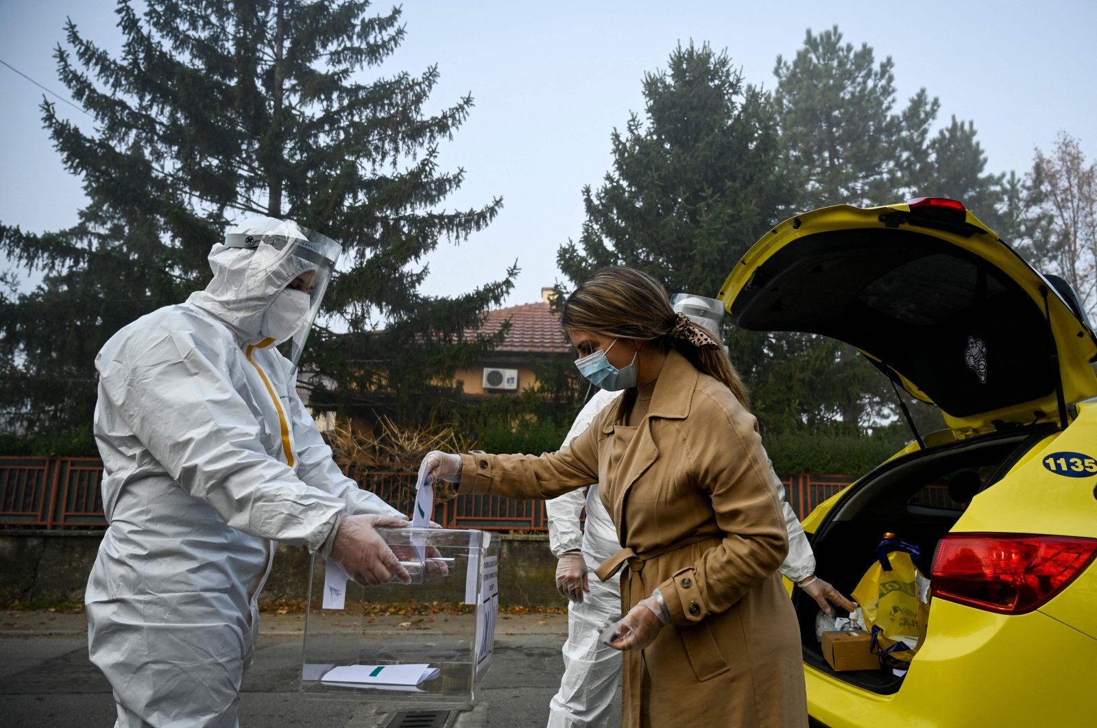 An electoral staff member of a mobile polling center, wearing Personal Protective Equipment (PPE), presents a ballot box to a woman in self-quarantine to collect her vote for the second-round of the presidential election and the parliamentary elections in the village of Voluek, Bulgaria, Nov. 21, 2021. (AFP Photo)