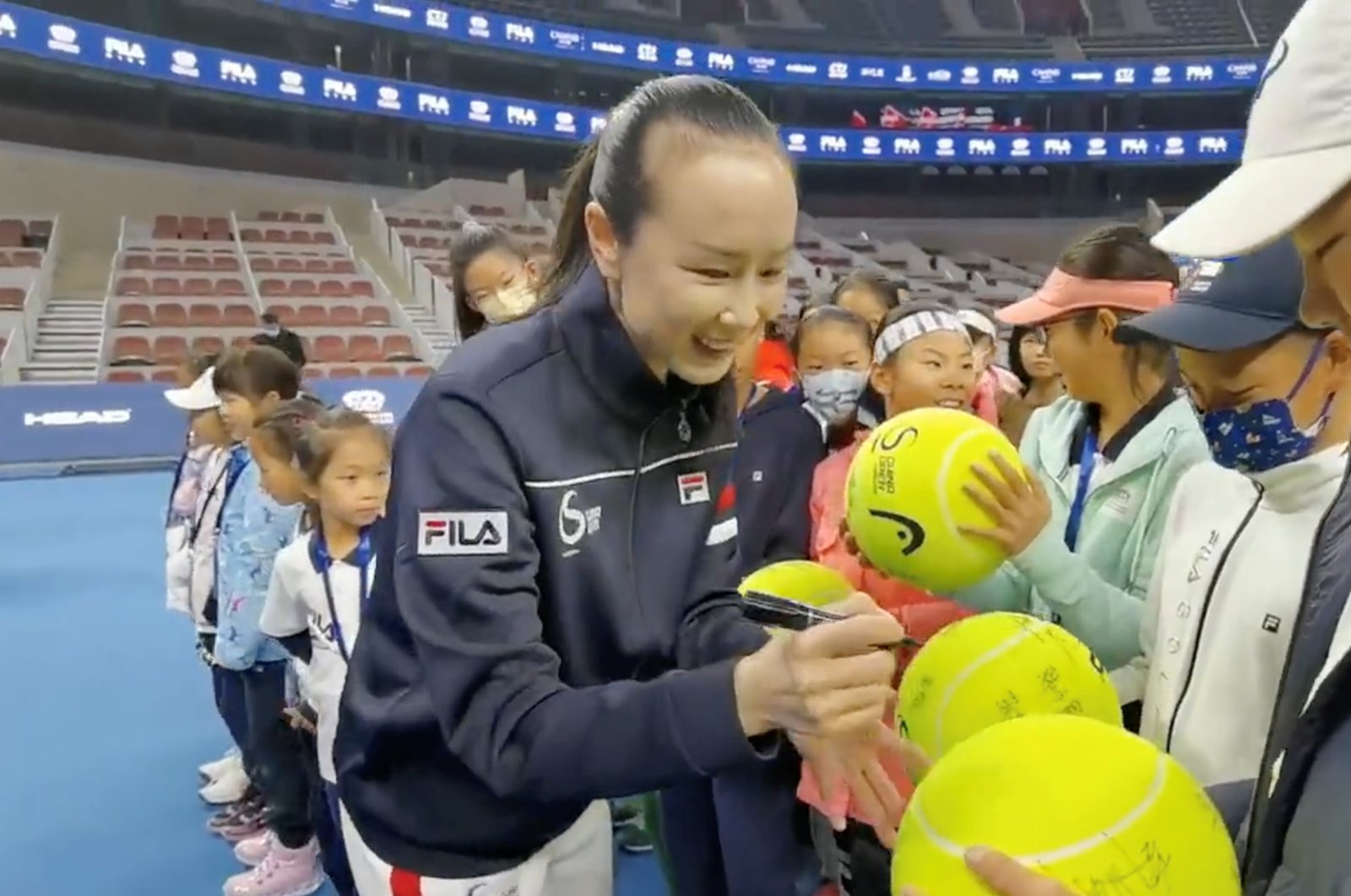Chinese tennis player Peng Shuai signs large-sized tennis balls at the opening ceremony of Fila Kids Junior Tennis Challenger Final in Beijing, China Nov. 21, 2021. (Twitter @Qingqingparis via Reuters)