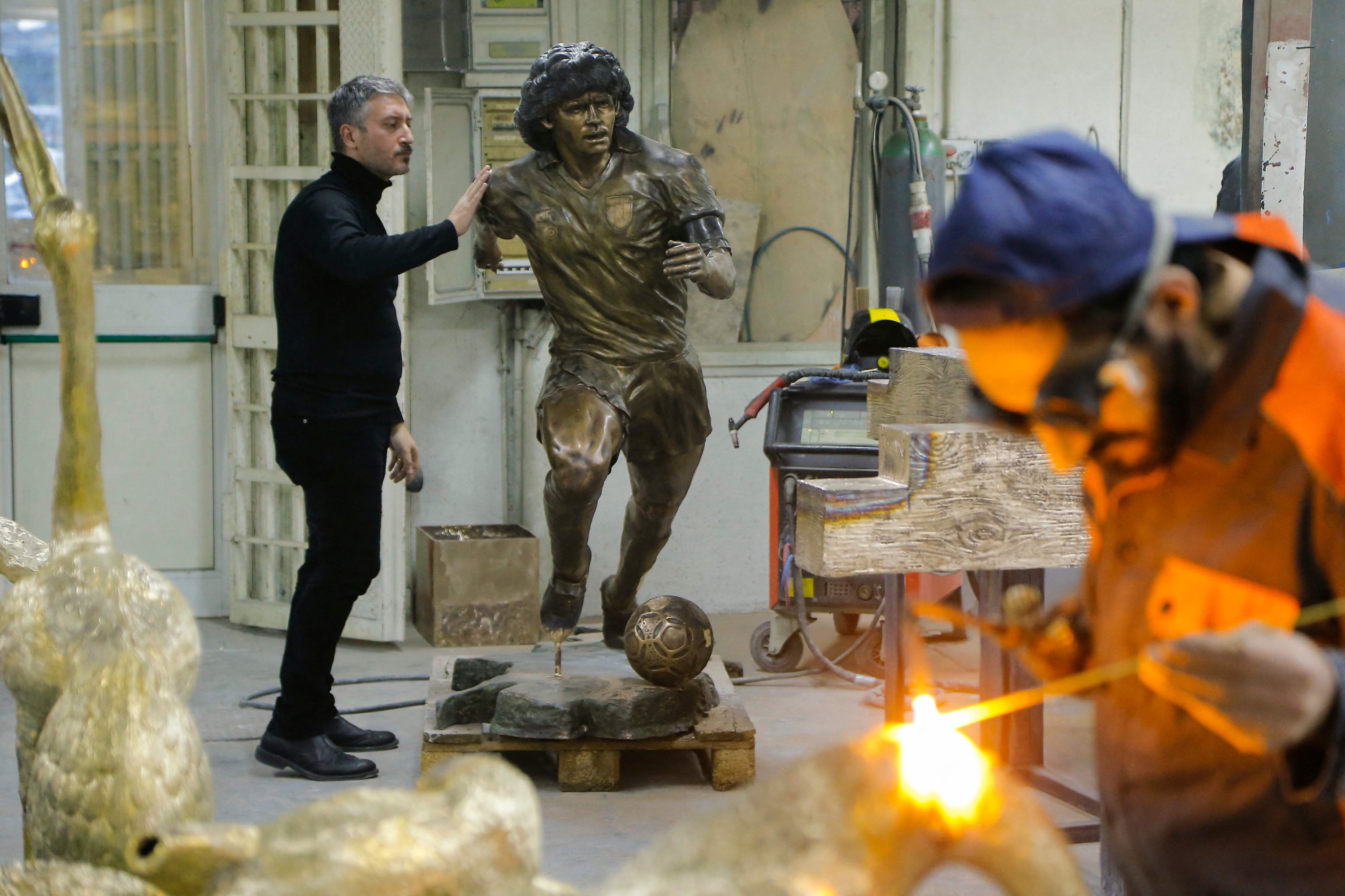 A welder works (R) as Italian sculptor Domenico Sepe touches a life-size bronze statue of the late Argentine football legend Diego Maradona, Naples, Italy, Nov. 22, 2021. (AFP Photo)
