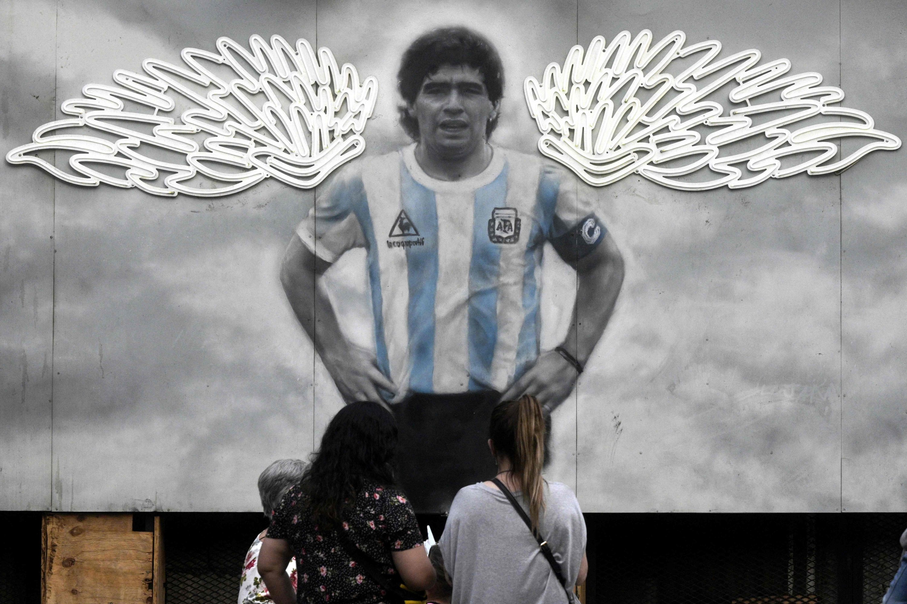 Women look at a mural depicting late Argentine football icon Diego Maradona, by artists Maximiliano Bagnasco and Dreier Salamanca Vargas, outside a restaurant in Buenos Aires, Nov. 4, 2021. (AFP Photo)