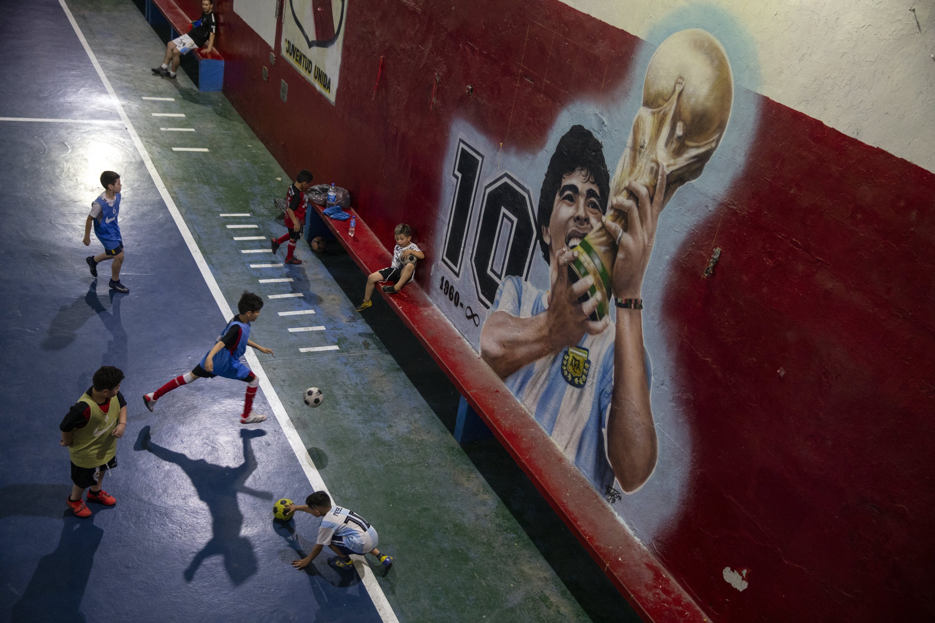 Children play football near a mural featuring the late football icon Diego Maradona in the 'Juventud Unida' club in Buenos Aires, Argentina, Nov. 24, 2021. (AP Photo)