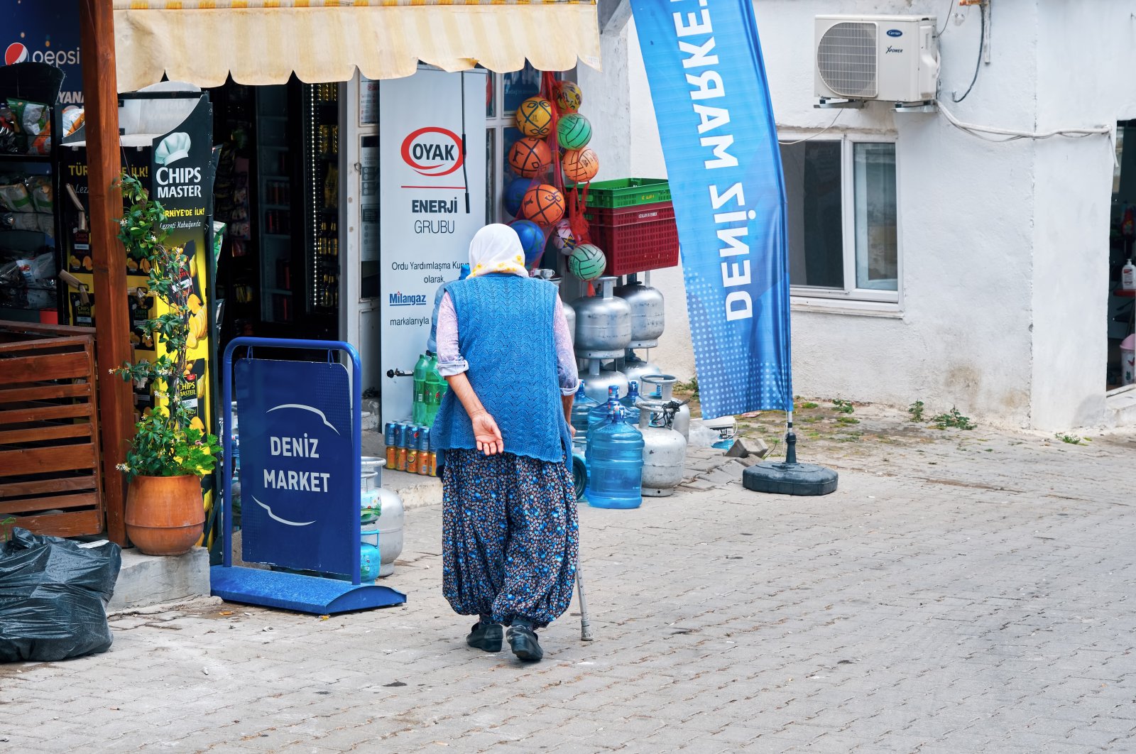 Elderly senior woman walks with her cane toward a rural market grocery wearing şalvar pants in Bademler village, Urla, Izmir, Turkey. (Shutterstock Photo)