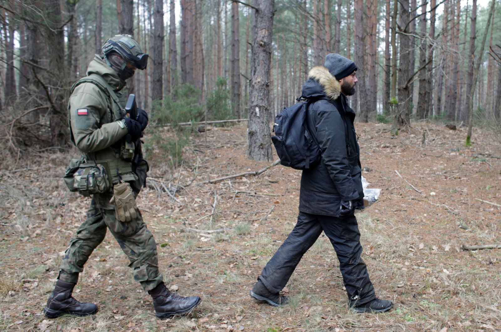 A soldier walks behind Iraqi migrant Salih Remitdh, 41, from Basra, who asked the border guards for international protection after being found in the woods by volunteers, close to the Milejczyce village, Poland, Nov. 26, 2021. (Reuters Photo)