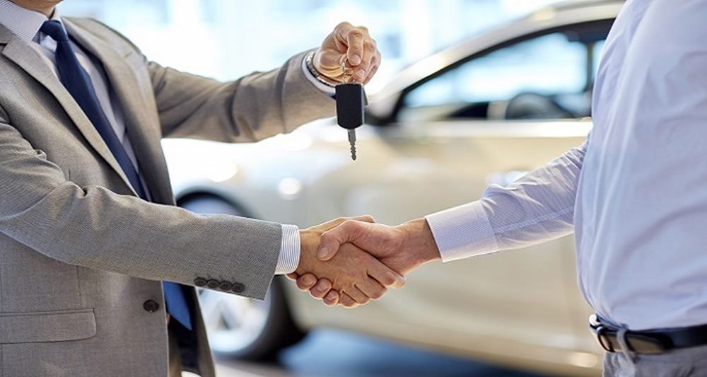 A dealer hands over car keys to a new owner and shakes his hand at an auto show. (Shutterstock Photo)