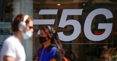 People wearing face masks walk past a 5G data network sign at a mobile phone store in Paris, France, April 22, 2021. (Reuters Photo)
