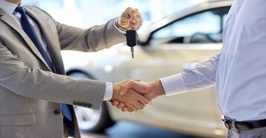 A dealer hands over car keys to a new owner and shakes his hand at an auto show. (Shutterstock Photo)