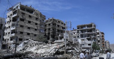 People stand in front of damaged buildings, in the town of Douma, the site of a suspected chemical weapons attack, near Damascus, Syria, April 16, 2018. (AP File Photo)